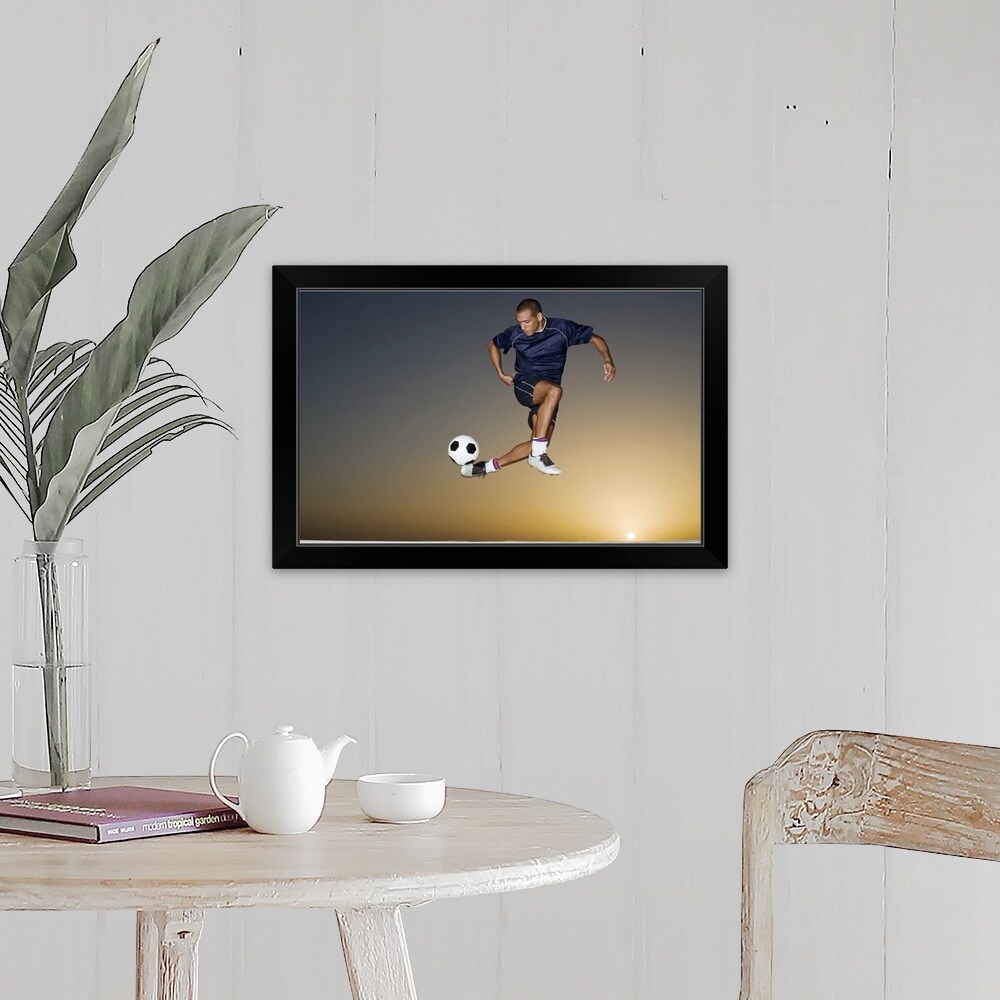 "Soccer player kicking ball in mid air" Black Framed Print